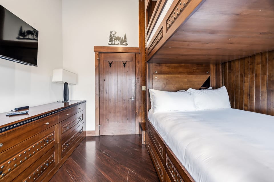 Bunk room with mounted TV and full bedding.