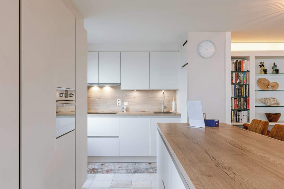 Modern open kitchen with ocean views. Features a sleek island, stylish barstools, and warm lighting, creating a bright and inviting space.
