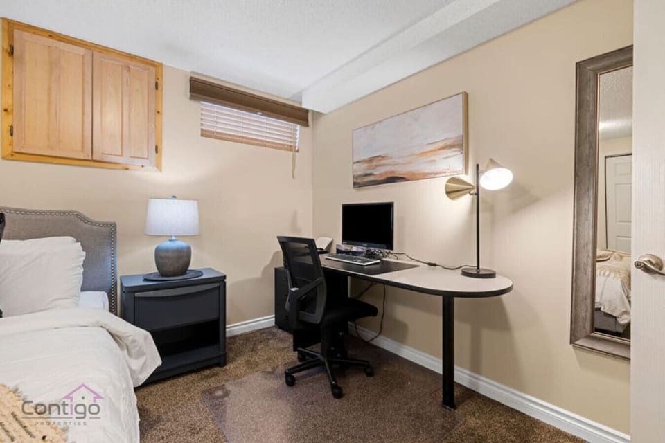 Relax and work in this functional king bedroom, featuring a bed, nightstand with lamp, desk with computer, office chair, and mirror.