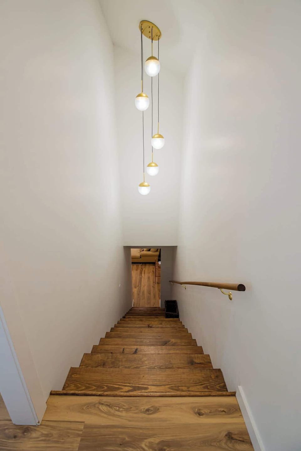 Navigate floors easily using this wooden staircase, illuminated by a multi-pendant brass light fixture hanging above.