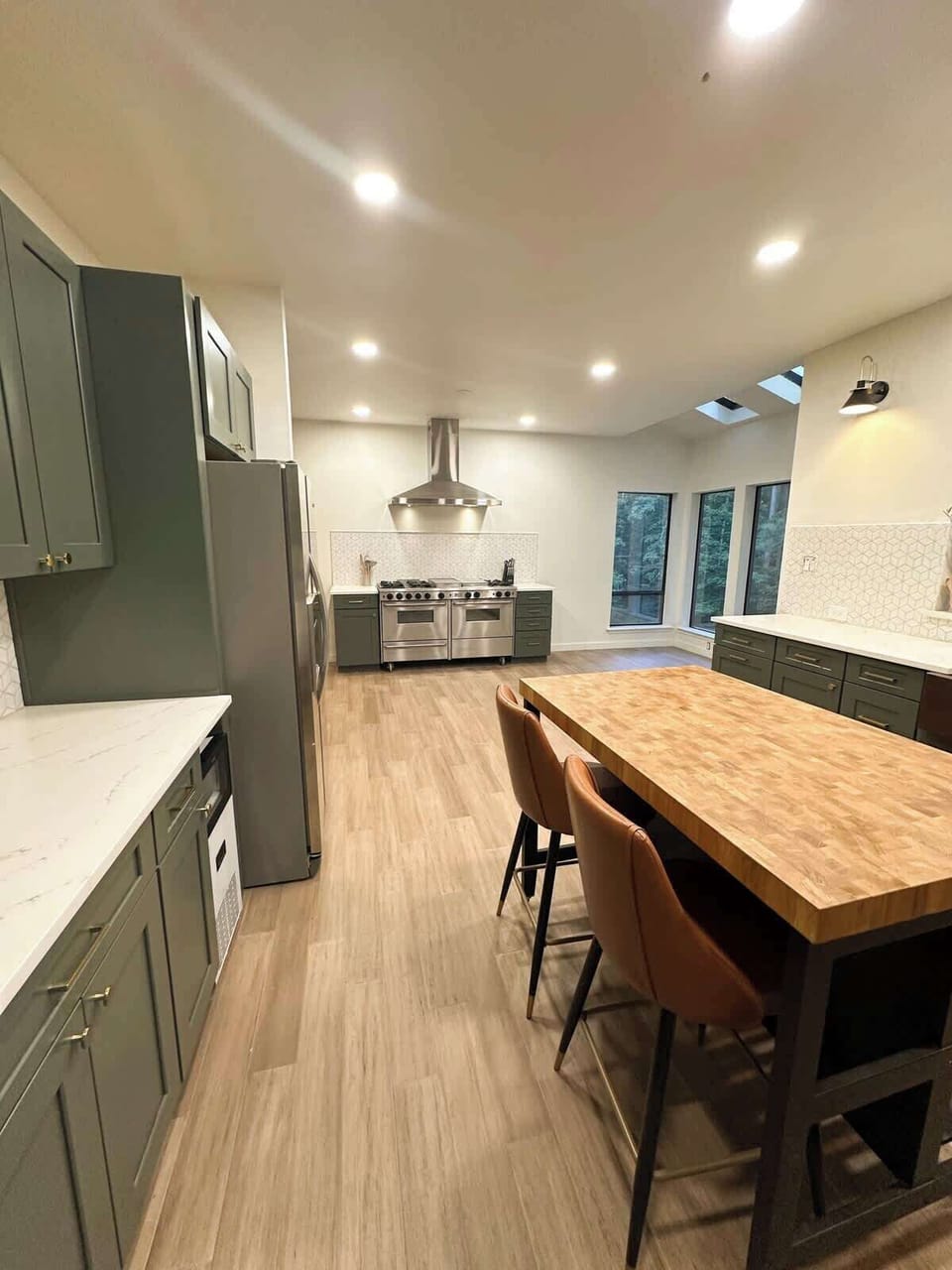Enjoy cooking and gathering in this spacious kitchen featuring sage green cabinetry, a butcher block island with leather barstools, stainless steel appliances, and bright recessed lighting.