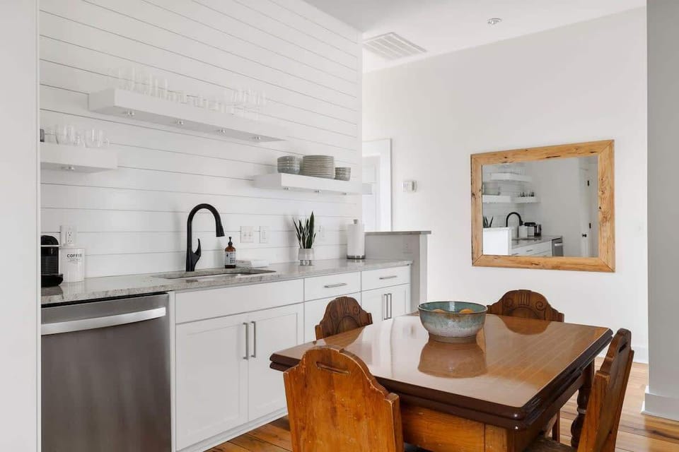 Enjoy meals or morning coffee in this bright space blending vintage charm with modern style—featuring open shelving, a sleek faucet, and a classic wood table perfect for gathering or working in comfort.