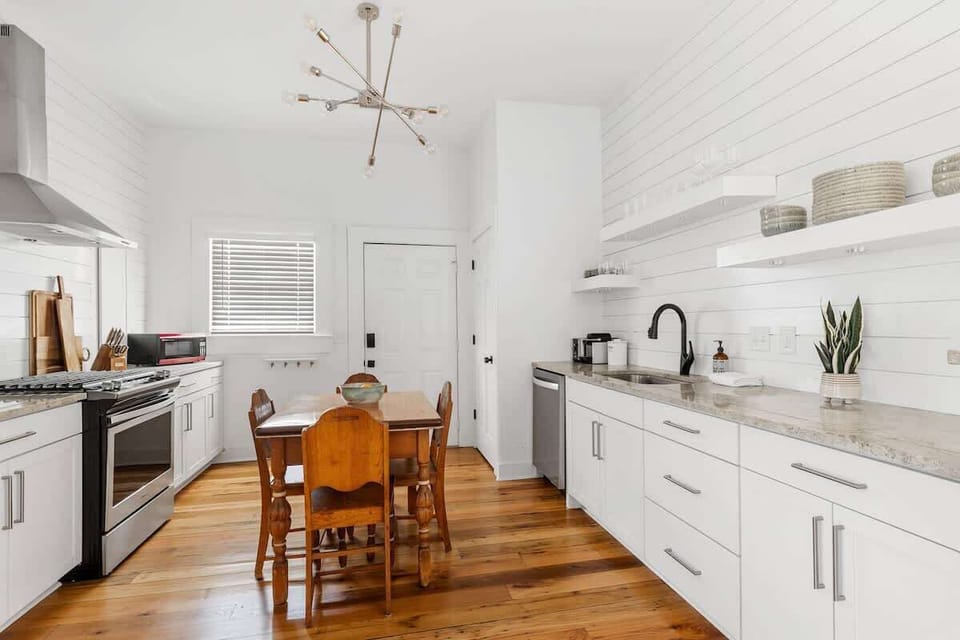 Gather around the rustic dining table or prep a meal in the sleek, white kitchen—featuring open shelving, modern fixtures, and everything you need to feel right at home in Charleston.