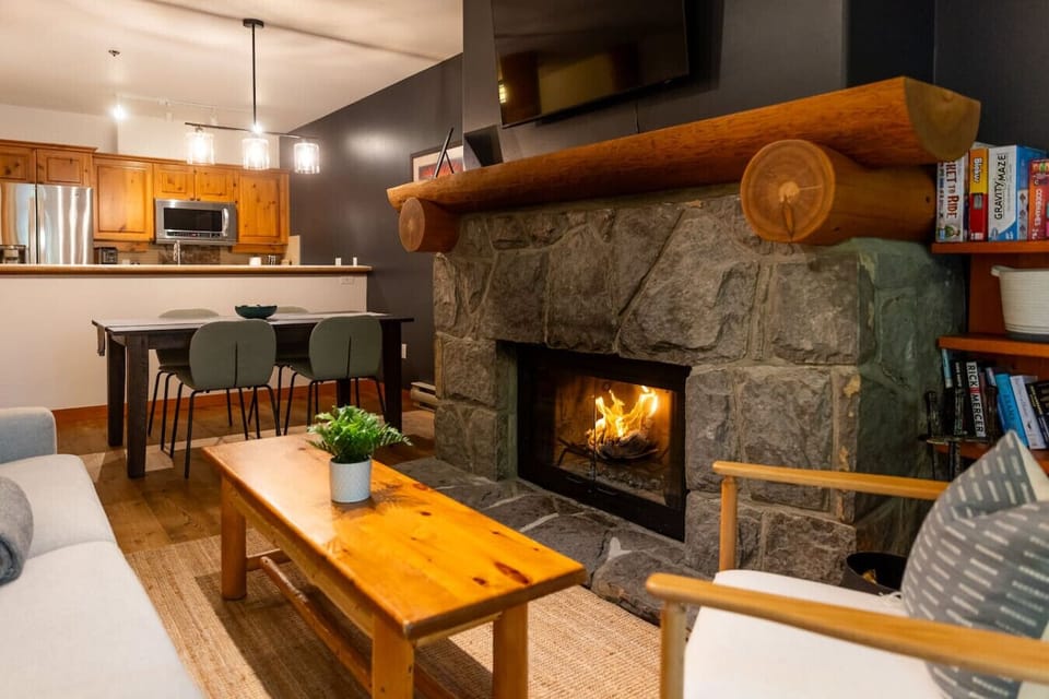 This cozy living space features a stone fireplacel, creating a warm and inviting atmosphere. The open layout connects the comfortable seating area with a modern kitchen and dining space, perfect for relaxing or entertaining guests.
