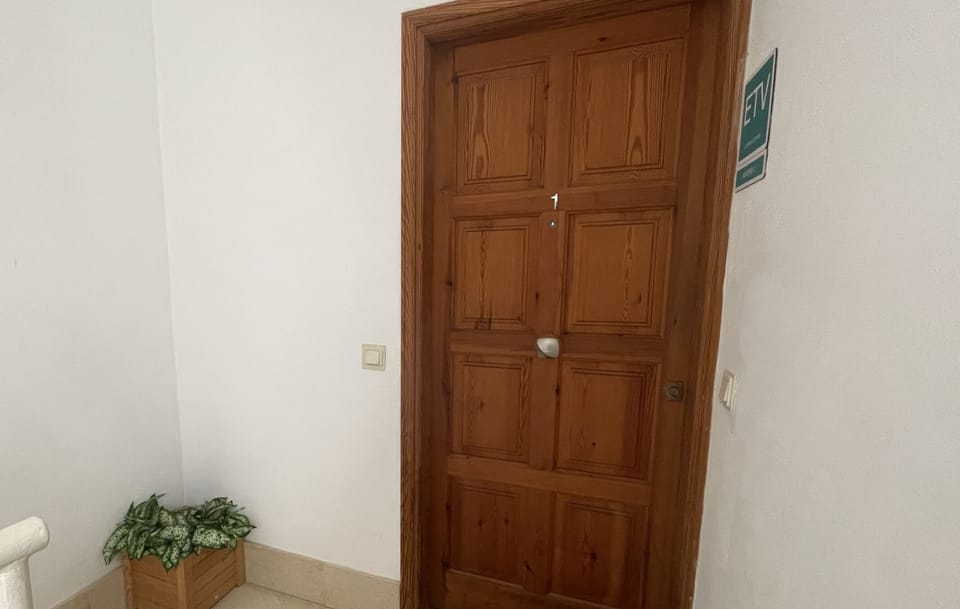 Apartment entrance with wooden door and bright shared hallway.