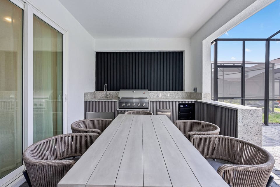 Experience our stylish outdoor dining area featuring a sleek wooden table and chic woven chairs, ideal for al fresco meals. With a modern grill and dark accent wall, it’s the perfect spot for leisurely evenings under the sky.