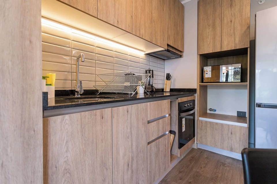 Sleek and modern kitchen with all essentials for a comfortable stay, featuring stylish wood cabinetry and ambient lighting.