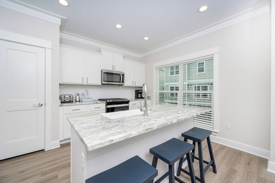 This modern kitchen features sleek white cabinetry, granite countertops, and a convenient breakfast bar with blue stools