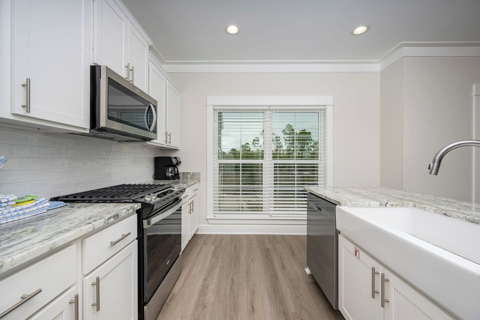 The kitchen features stainless appliances, granite countertops, modern upgrades, and a window view of lush greenery