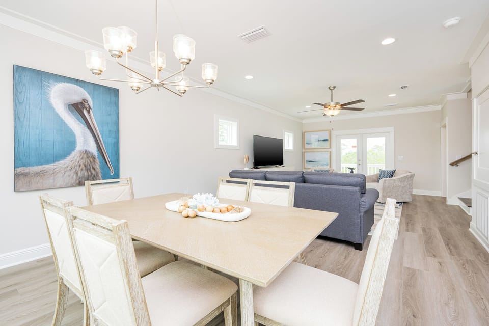 The living and dining space features cozy seating, a large TV, and a charming pelican artwork, perfect for relaxation