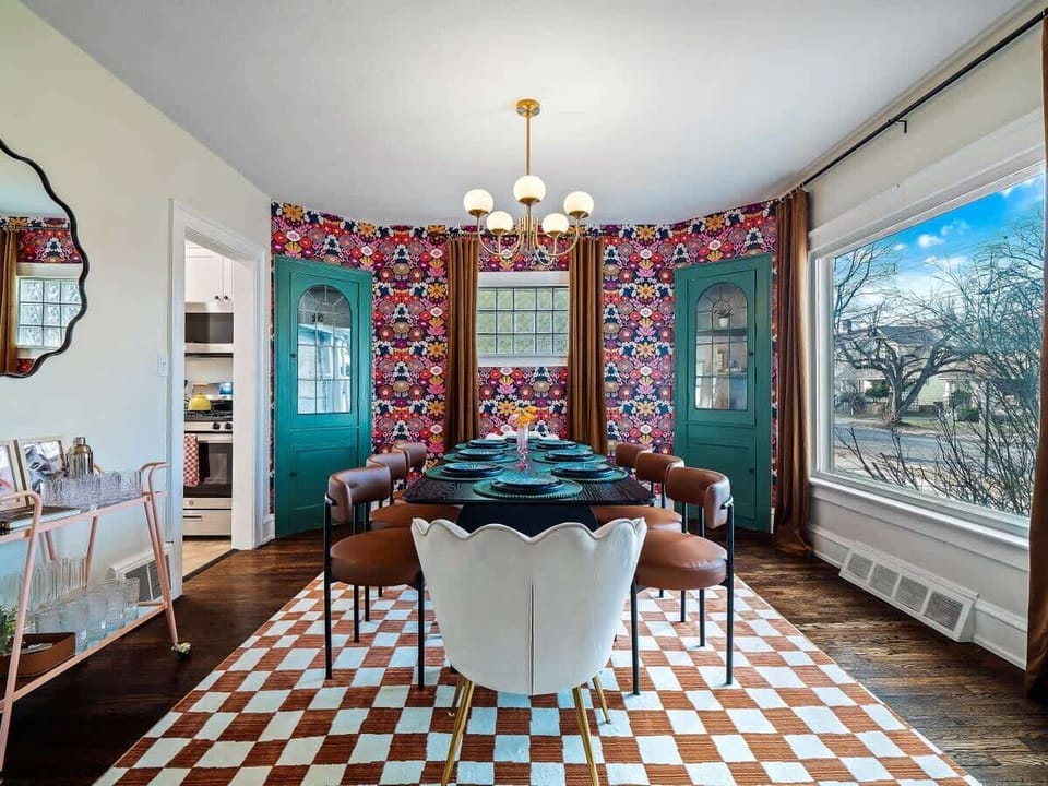Eclectic dining room w/ patterned chairs, bright artwork & windows that fill the room w/ light