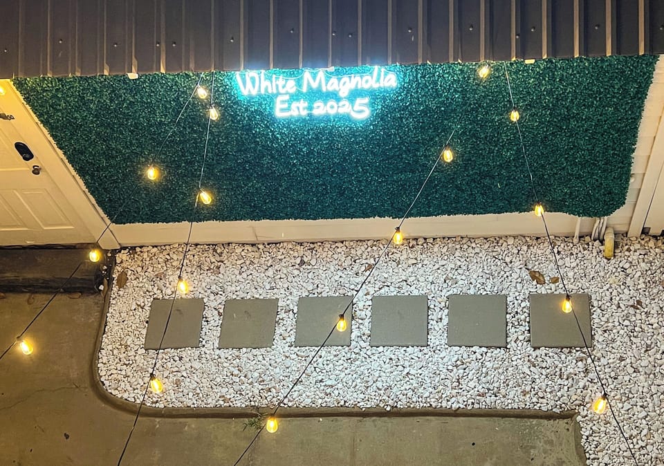 Lighted photo wall in private courtyard with white magnolia neon sign