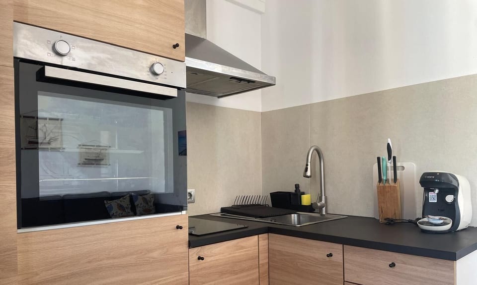 Modern and functional kitchen with wood finishes, equipped with oven, hob, coffee machine and basic utensils, ideal for holiday stays in Puerto Pollensa.
