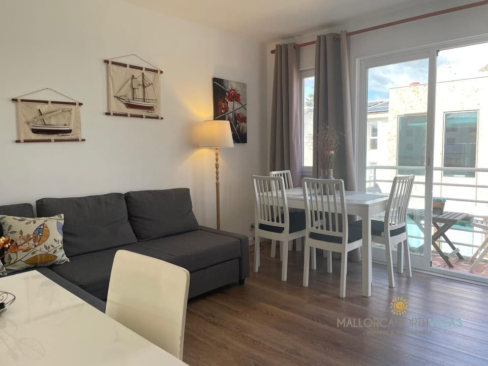 Bright living-dining room featuring a corner sofa, white table with matching chairs, and nautical-themed wall decorations, creating a cozy coastal ambiance.