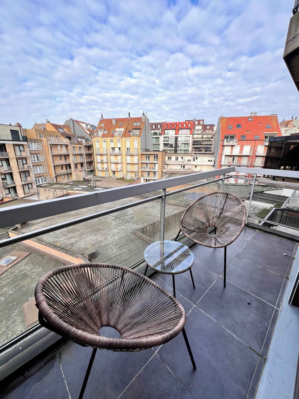 Sunny balcony with two lounge chairs and an open city view
