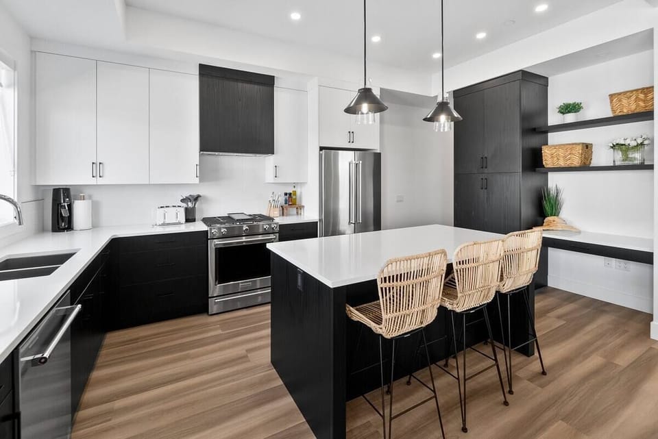 Modern kitchen and dining area with dark cabinetry, stainless steel appliances, and a spacious kitchen island with bar stools, ideal for cooking and entertaining.