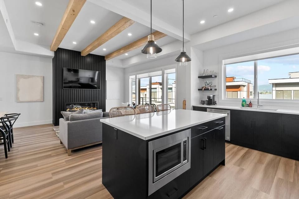Sleek kitchen with dark cabinetry, stainless steel appliances, and a spacious island, brightened by natural light in an open-concept layout.
