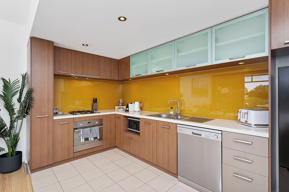 Create culinary delights in a modern kitchen, showcasing sleek cabinetry and a vibrant yellow backsplash.