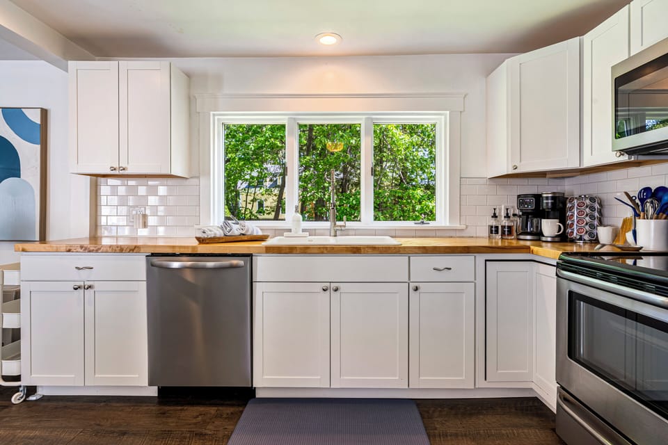 Bright white kitchen with wooden counters and a view of green trees.
