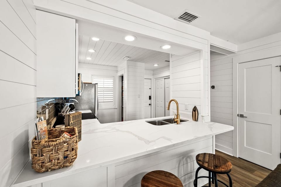 Your bright coastal kitchen awaits with gleaming marble counters, gold accents, and charming shiplap walls that make cooking feel like a seaside retreat.
