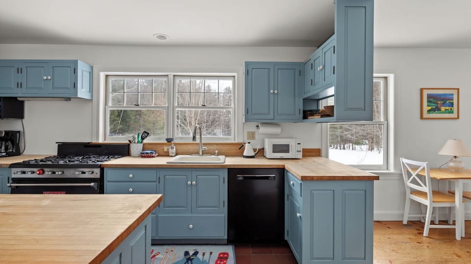 - Bright kitchen with natural light and forest views from wide windows   - Blue cabinets with wood countertops create a cozy cooking space   - Fully stocked kitchen with dishwasher and appliances for guests