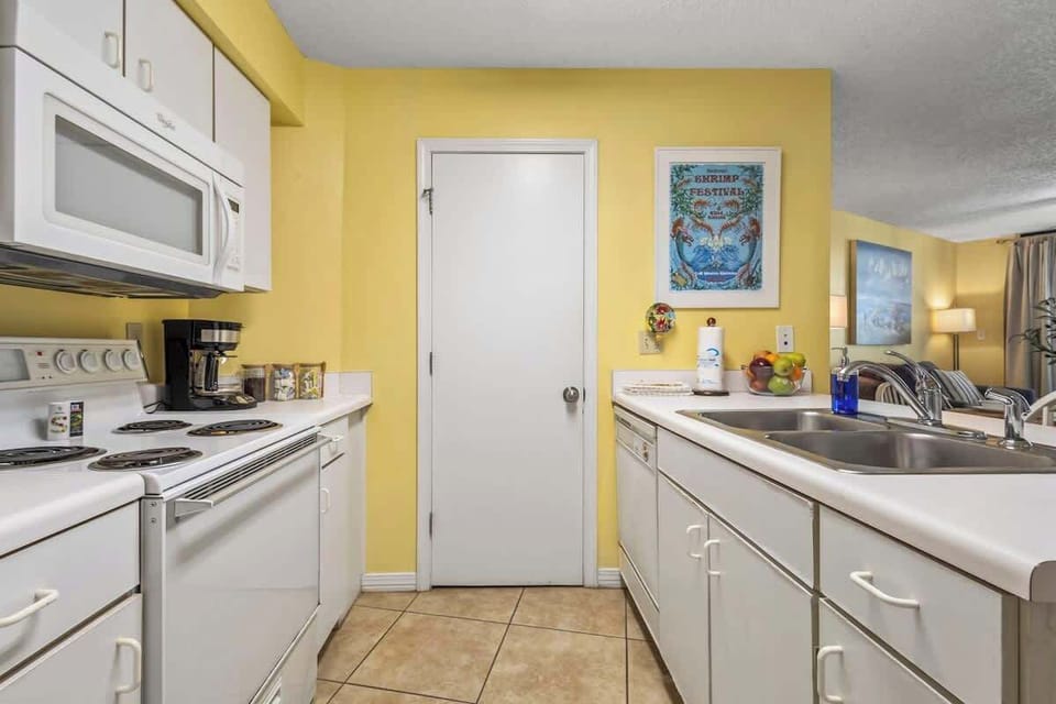 The open kitchen seamlessly flows into the dining and living areas, creating the perfect space for entertaining. A large counter with a sink, bright lighting, and beachy decor make it a welcoming spot for meals and gatherings.