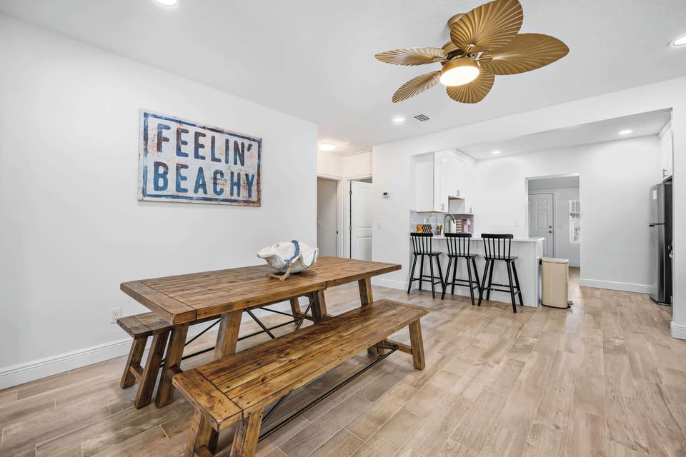 Rustic wooden dining table with bench seating adjacent to a modern kitchen bar with black stools.