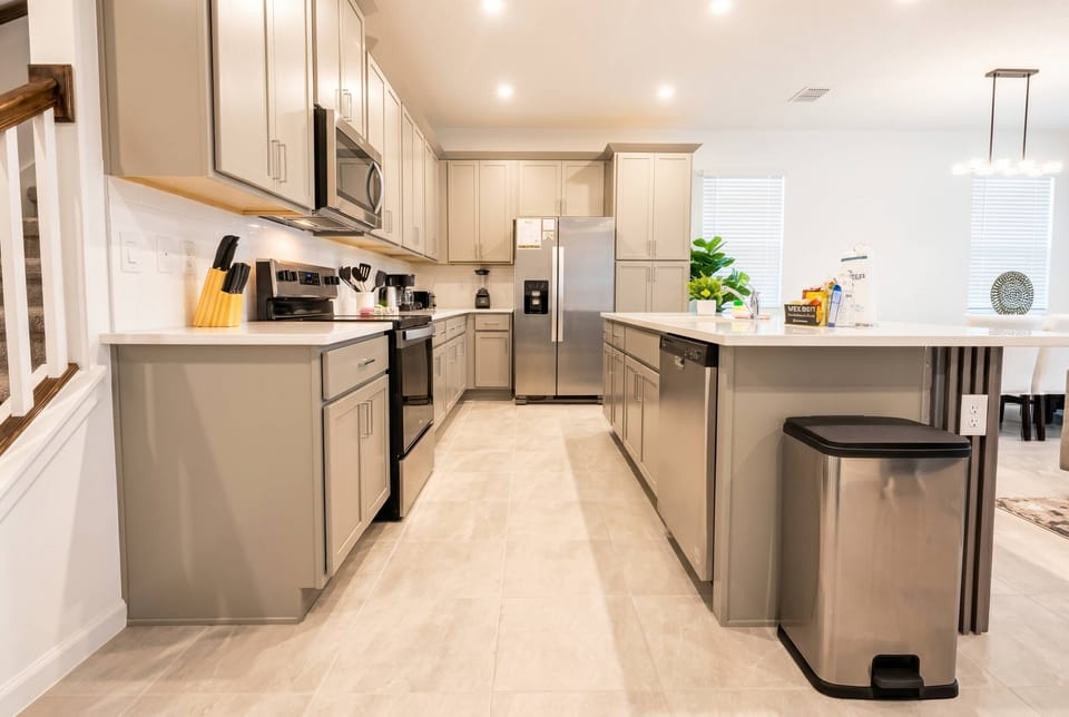 Enjoy cooking in this stylish kitchen with light-gray cabinetry and modern stainless steel appliances. The spacious island is perfect for casual meals or morning coffee, and the warm lighting creates an inviting atmosphere.