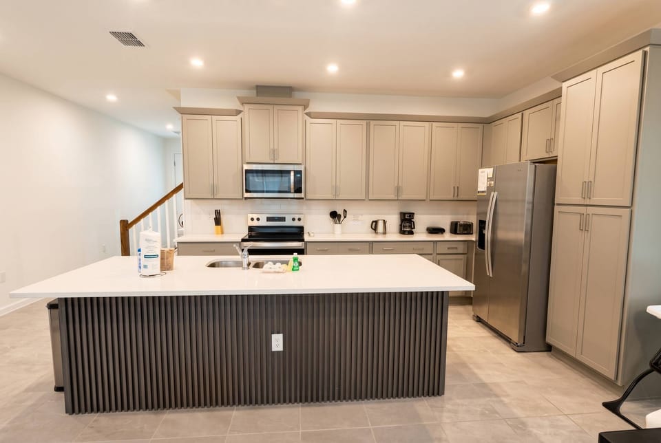 Experience this stylish kitchen with light gray cabinetry and a spacious island that inspires culinary creations. Modern appliances and bright recessed lighting set the perfect scene for cooking and gatherings with loved ones.