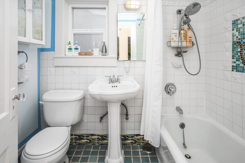 Salmon-print floor tiles, a scalloped pedestal sink, and a handmade mermaid mosaic in the shower — this ocean-themed full bath is the kind of playful detail that makes the whole house feel considered rather than generic.