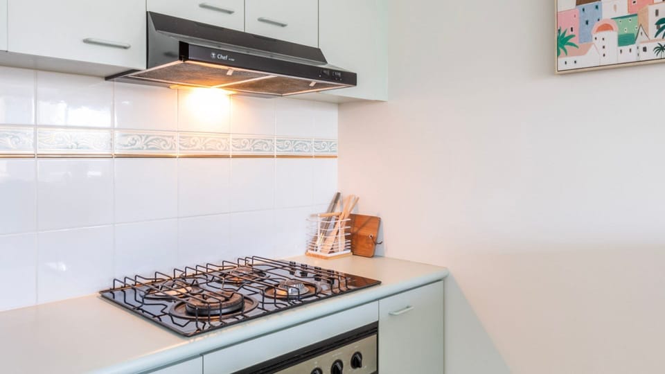 A contemporary chef's corner featuring a premium stainless steel cooktop, overhead rangehood, and crisp white splashbacks.
