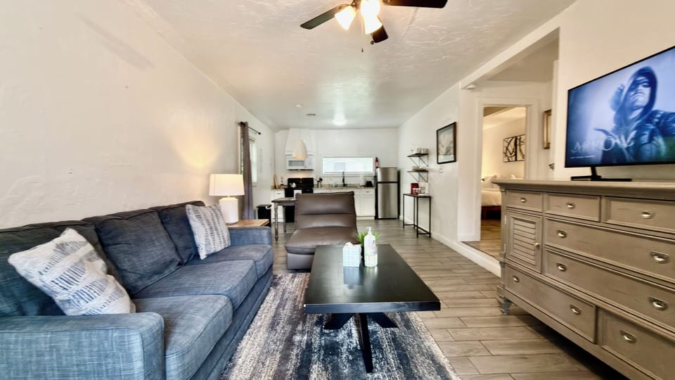Relax in a stylish living room with a comfy sectional, smart TV, and seamless flow into a modern kitchen—perfect for unwinding or entertaining.