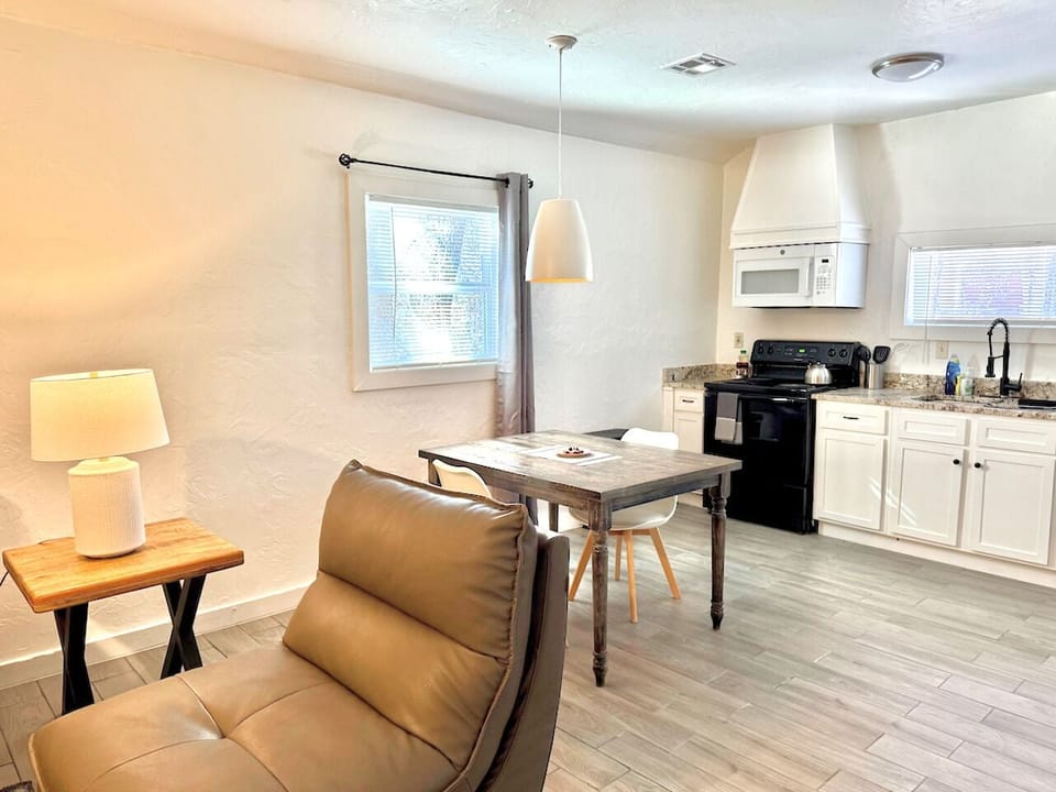 A bright and modern open-concept space featuring a rustic dining table and a fully equipped kitchen with sleek white cabinetry and updated appliances.