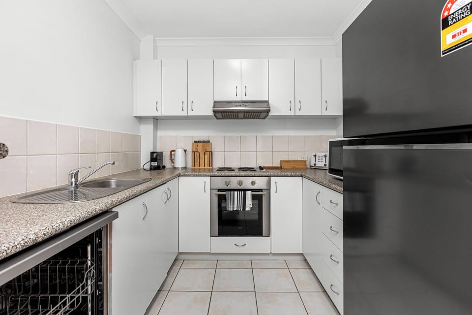 Prepare meals with ease in a bright white kitchen, equipped with modern appliances and a sleek black refrigerator.