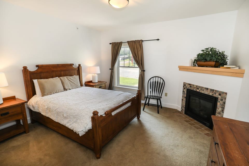 Bright bedroom with a comfortable bed, fireplace, and large window for natural light.