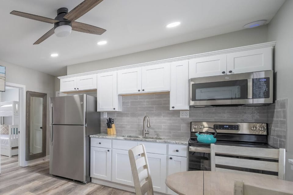 Bright, modern kitchen with stainless steel appliances, sleek white cabinetry, and a cozy dining area. Fully stocked for home cooking, with ample counter space and stylish finishes for a comfortable stay.