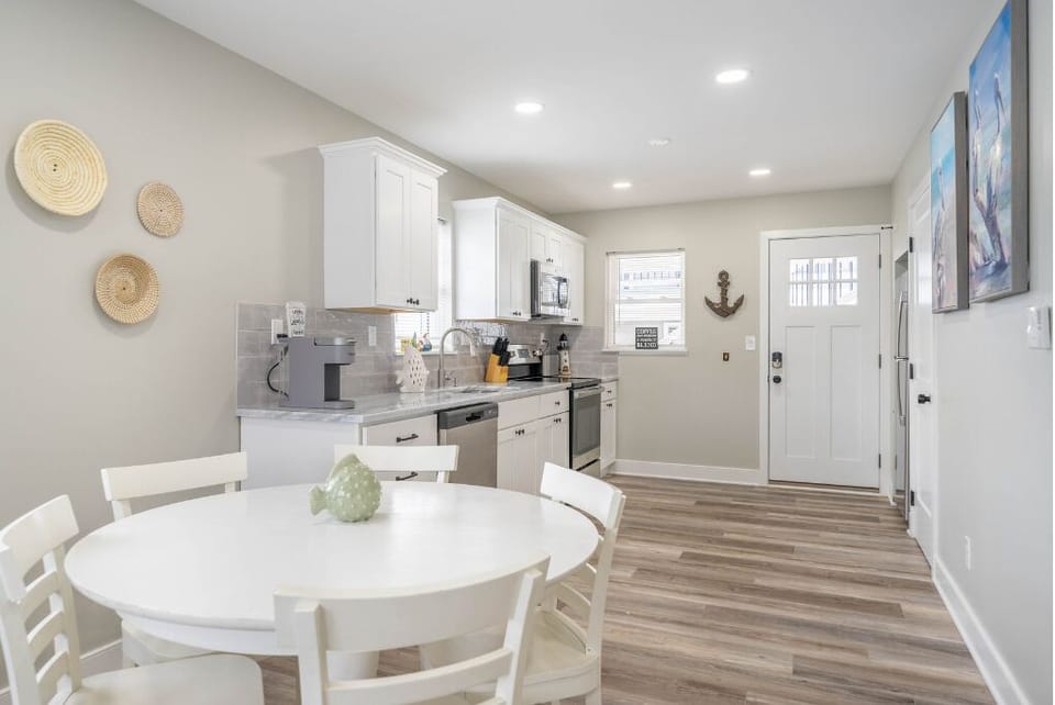 A bright, coastal-inspired kitchen and dining space featuring modern appliances, soft gray tones, and charming wall décor. Perfect for sharing meals, relaxing, and enjoying a clean, inviting atmosphere.