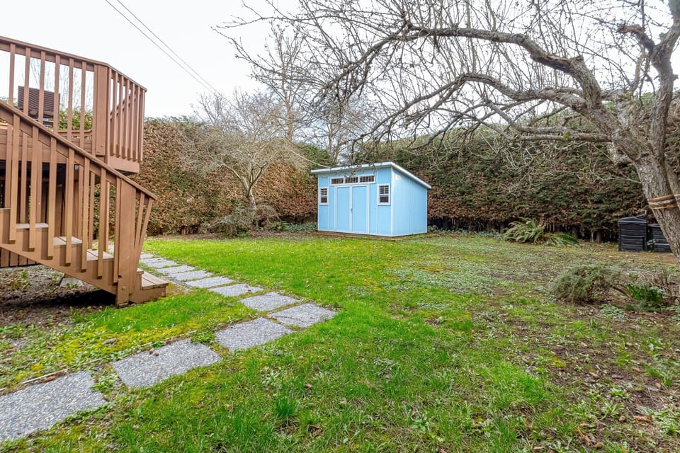 Garden area with stepping stone path, brown wooden staircase, leafless trees, and a small blue shed.