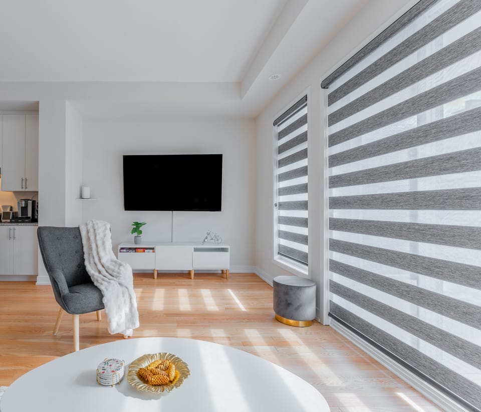 A modern living room with a plush gray chair, white throw, and TV setup.