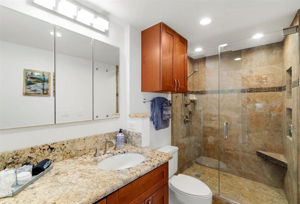 Start your mornings or unwind after a beach day in this beautifully updated bathroom. It features a spacious granite vanity with plenty of room for your essentials, along with a luxurious, glass-enclosed walk-in shower showcasing gorgeous stone tile work.