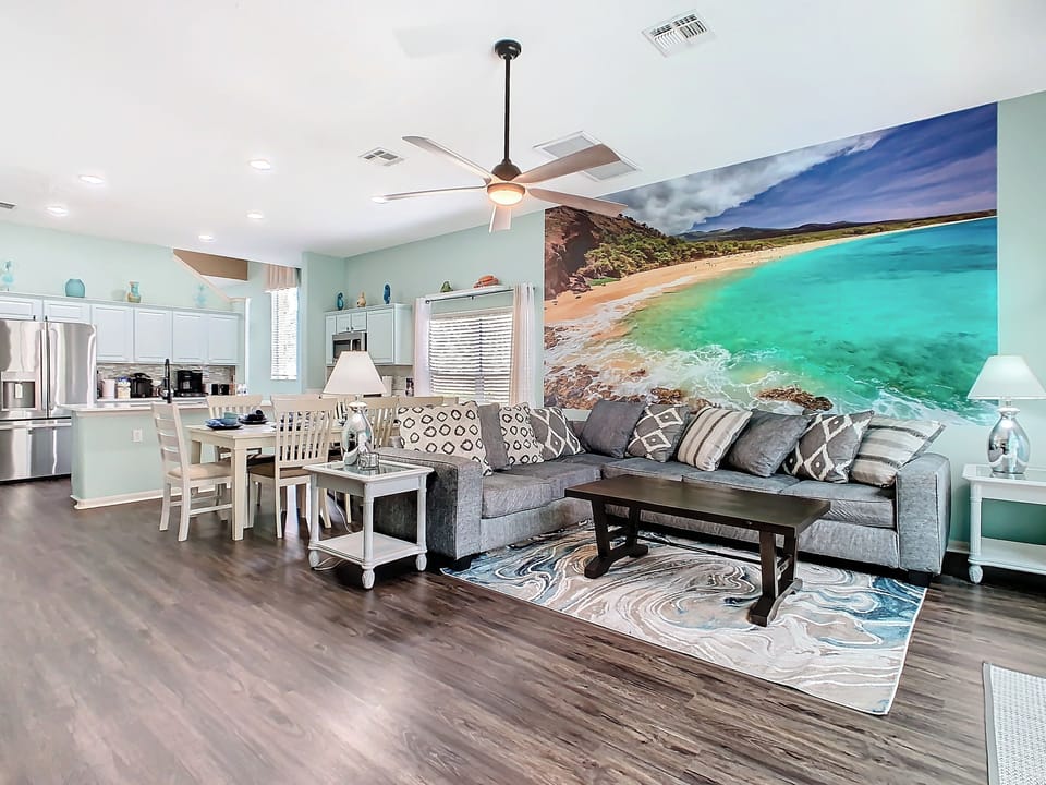 - Spacious open layout with a large beach mural that adds a serene coastal vibe
- Plush gray sectional and patterned pillows offer comfy seating for the whole group
- Full kitchen, dining set, and ocean toned decor perfect for gathering and relaxing