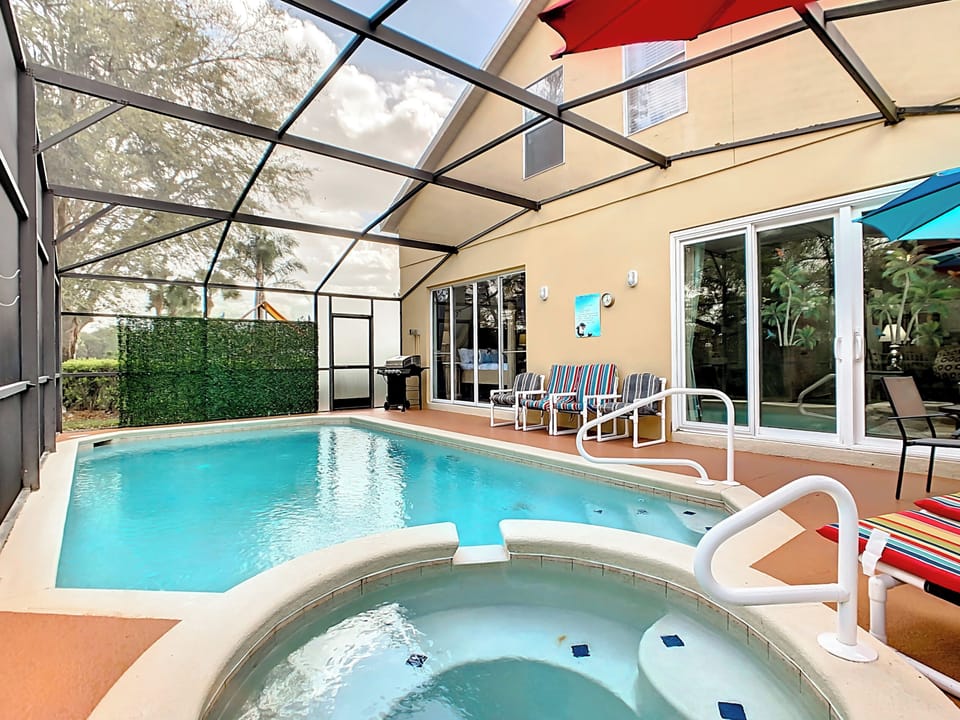 This serene backyard oasis features a crystal-clear pool, a round hot tub with blue mosaic tiles, and vibrant lounge chairs under colorful umbrellas. A sleek black grill stands ready for gatherings, while a lush privacy screen enhances seclusion. The robust screen enclosure lets in light while keeping pests out, creating the perfect space for relaxation and entertainment.