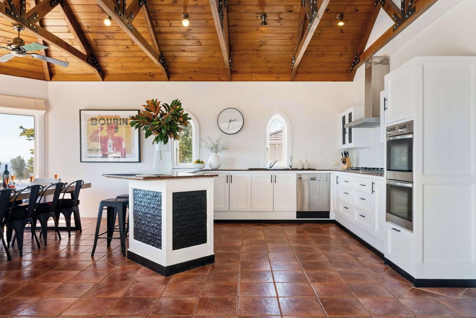 The indoor dining area, with large, gable ceilings. Space includes a dining table with ocean views and fully equipped kitchen