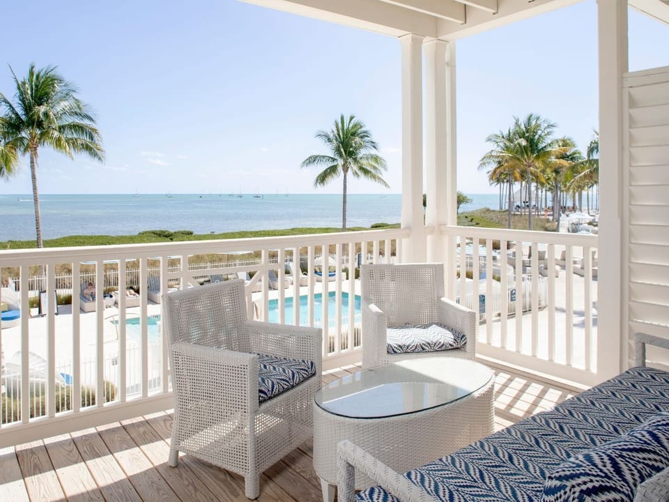 Relaxing balcony space with cozy seating and panoramic views of palm trees and the ocean.