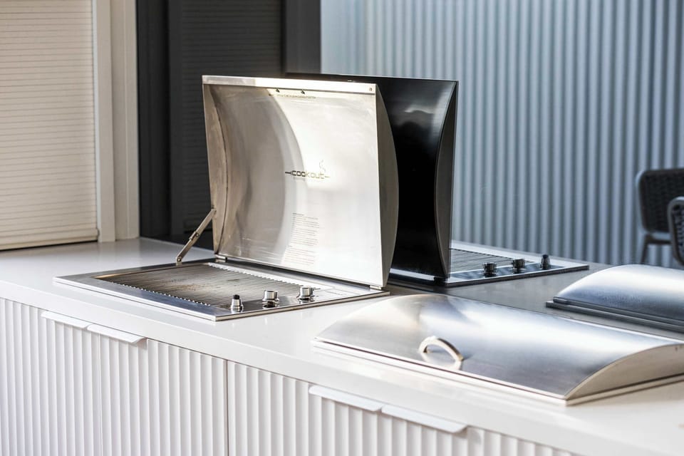 BBQ GRILL STATION I This photo showcases a sleek outdoor BBQ grill station, perfect for cooking and entertaining. The stainless steel grill is open and ready for use, set against a modern, corrugated backdrop. 
