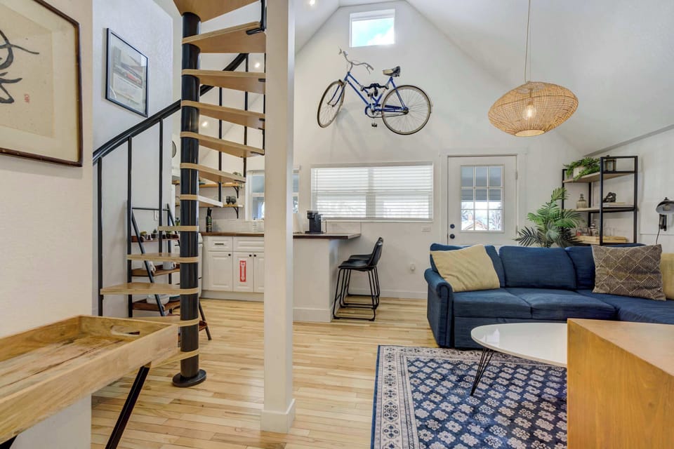 This bright and airy upstairs loft features an open-concept living area, high ceilings, and a stylish spiral staircase leading to the cozy sleeping space.





