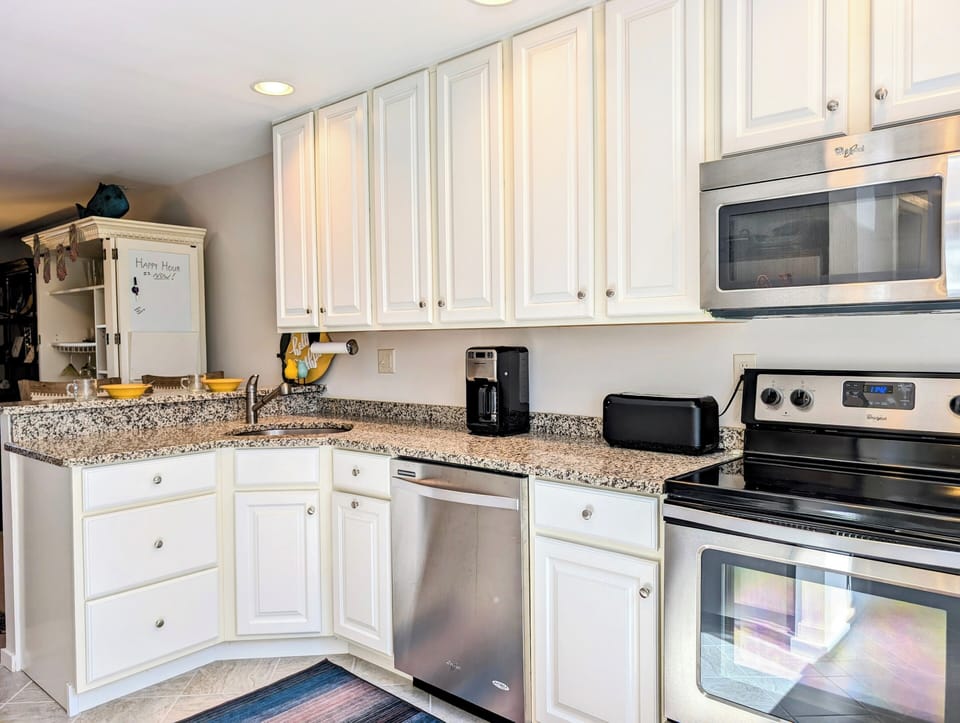 719A Treetop Lane - Kitchen Utility View - Modern kitchen featuring white shaker cabinets, stainless steel dishwasher and stove, granite countertops, and a subway tile backsplash with bright natural light from the window.