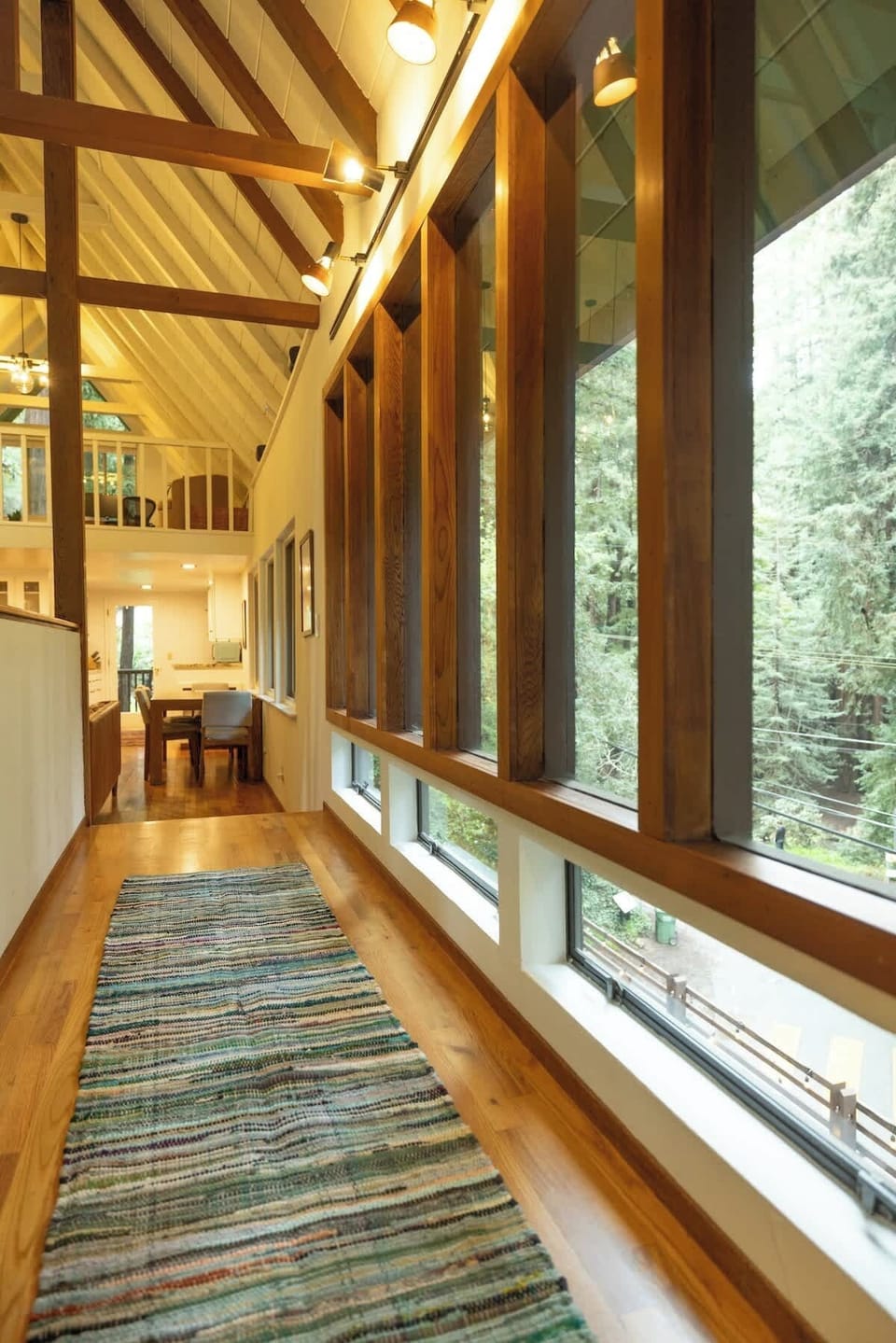 A sunlit corridor lined with expansive windows and warm wood accents creates a bright, airy passage that beautifully connects the home’s living spaces