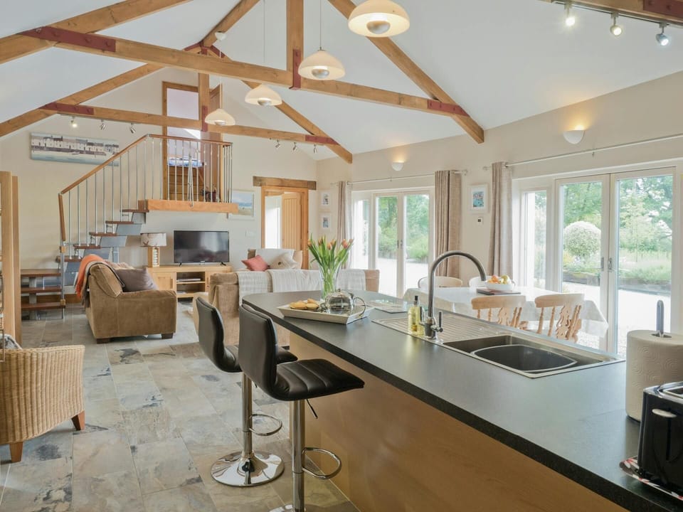 Open plan kitchen/living room: breakfast bar with sink and two bar stools