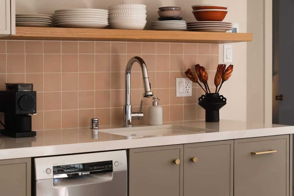A thoughtfully styled kitchen nook with warm tile backsplash, open wood shelving, modern fixtures, and sleek cabinetry offers a cozy and functional space for effortless meal prep